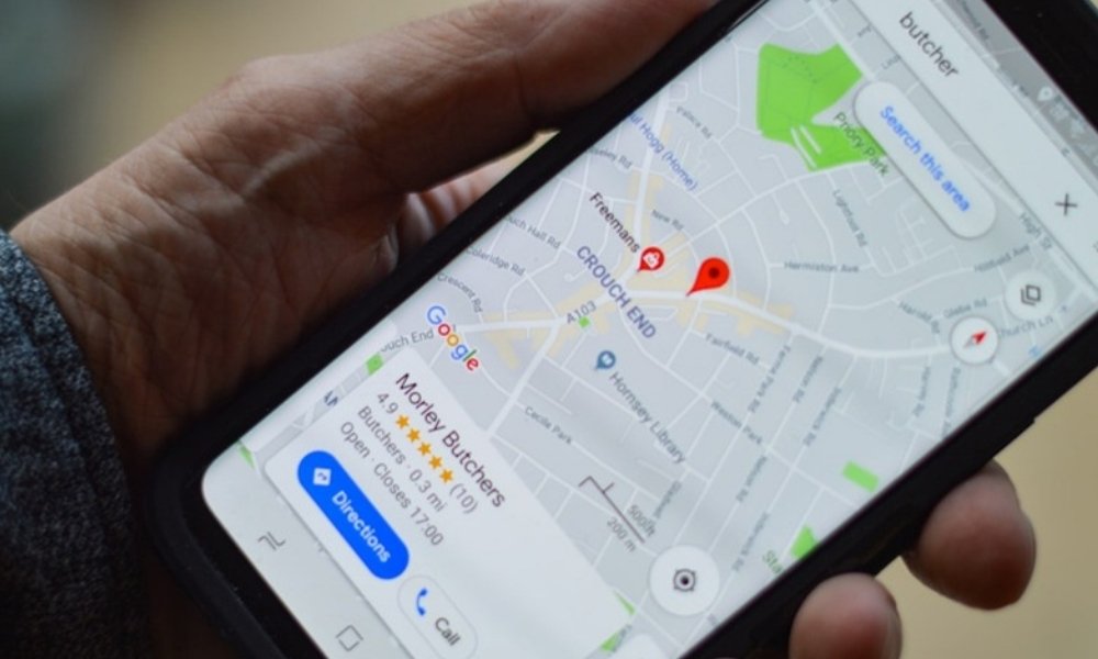 A hand holding a smartphone displaying a Google map with a local business search visible