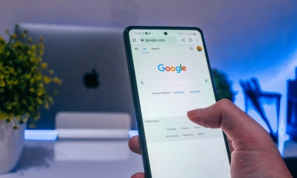 A hand holding a phone with the Google search bar open