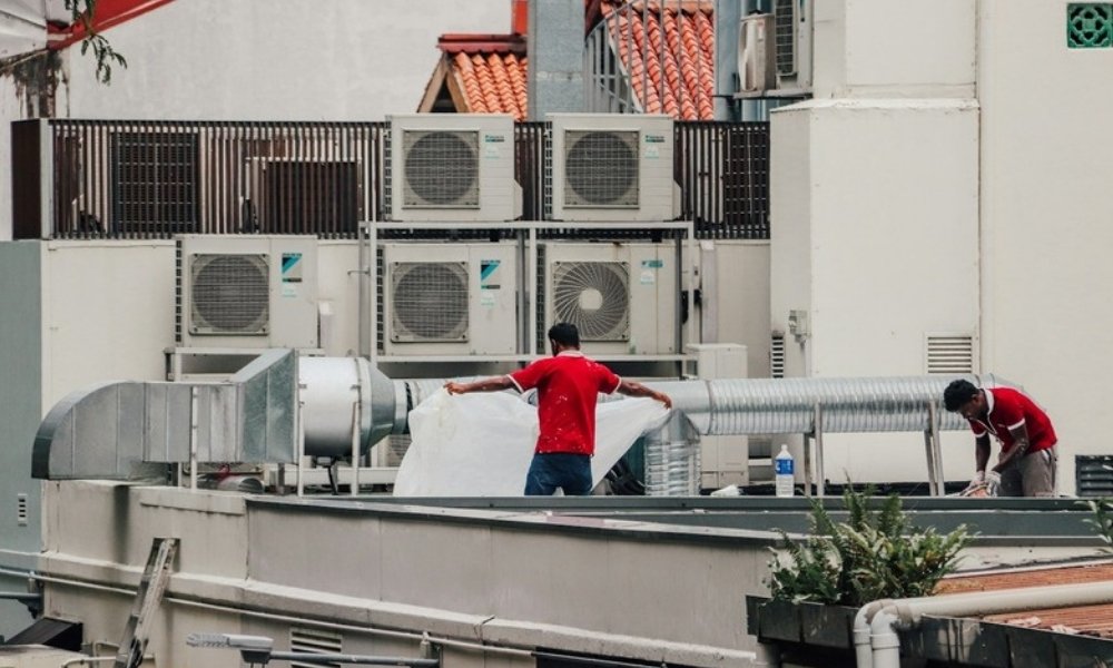 Two HVAC technicians working on commercial air conditioning units on a rooftop