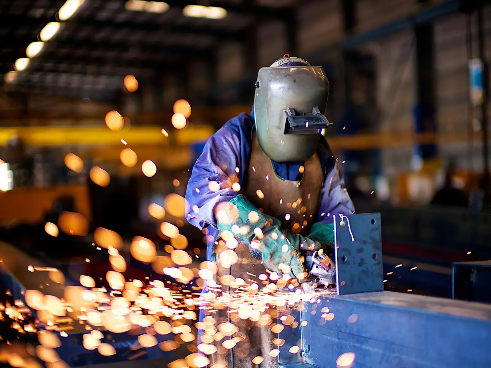 A DC Installations welder grinding a steel beam, sparks flying across the workshop